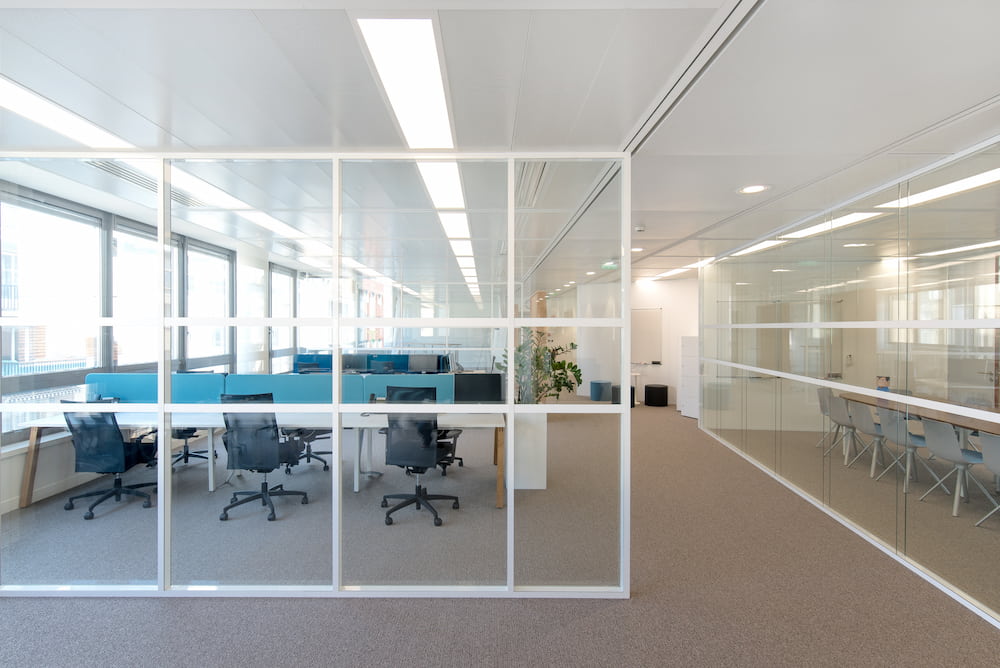 Bureau professionnel avec des espaces de travail et une salle de réunion. Le bureau est lumineux grâce à ses vitres transparentes qui laissent entrer la lumière.