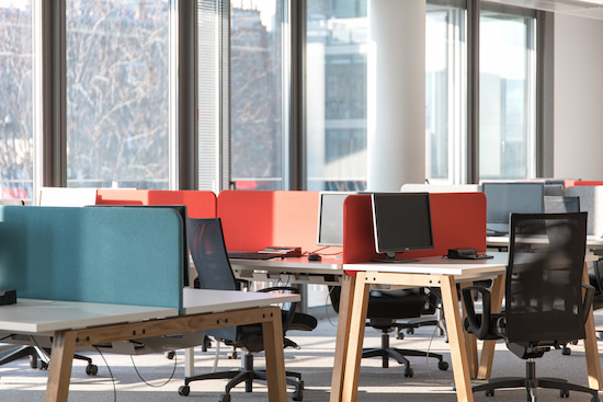 Aménagement d'un espace de travail en flex office avec des cloisons acoustiques colorées sur les bureaux bench et des chaises ergonomiques noires